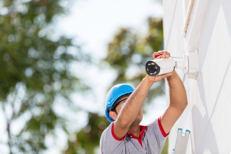A man wearing a hard hat and safety vest is installing a camera on a wall, ensuring safety and proper placement.