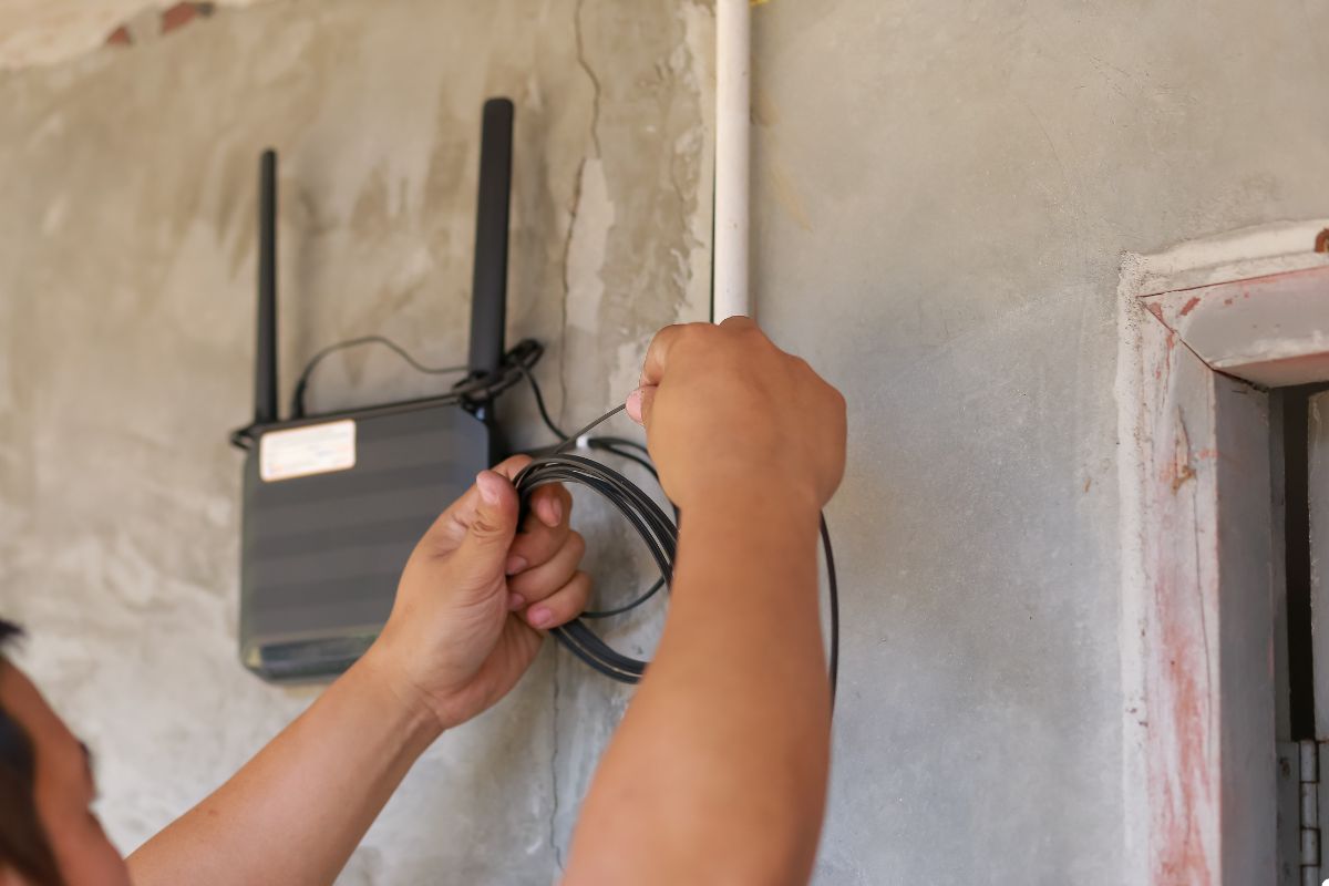 A person is securely mounting a wireless router onto a wall for improved internet connectivity. 