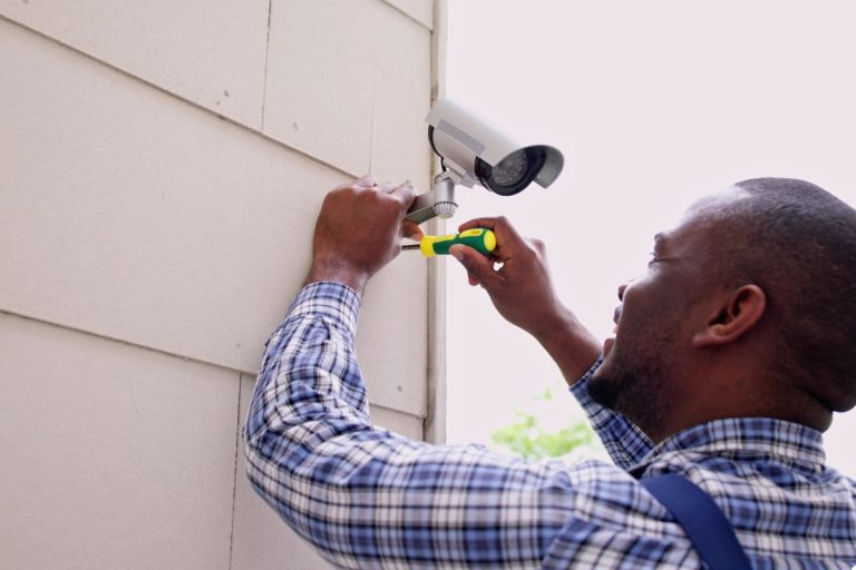 A man is installing a camera on a wall, ensuring it is securely fixed and properly oriented for surveillance purposes.