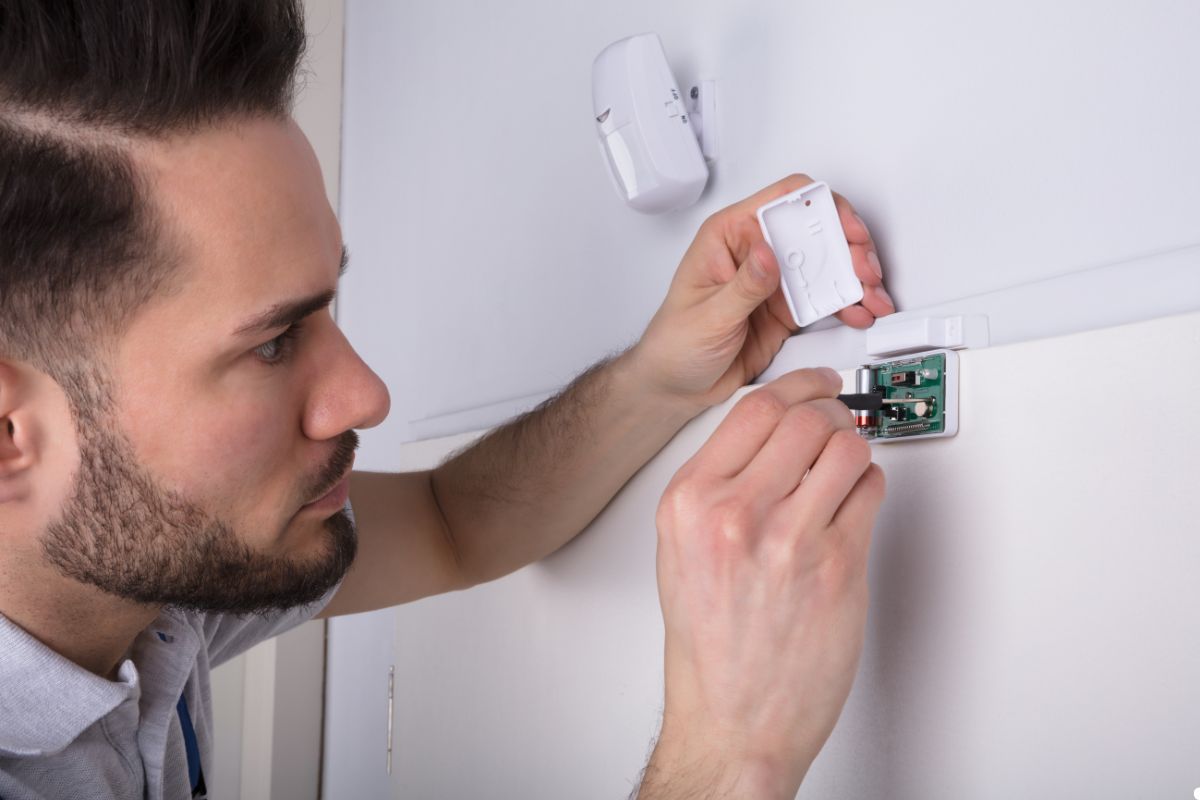 A man repairs a wall-mounted electronic device, using tools and focused on the task at hand.