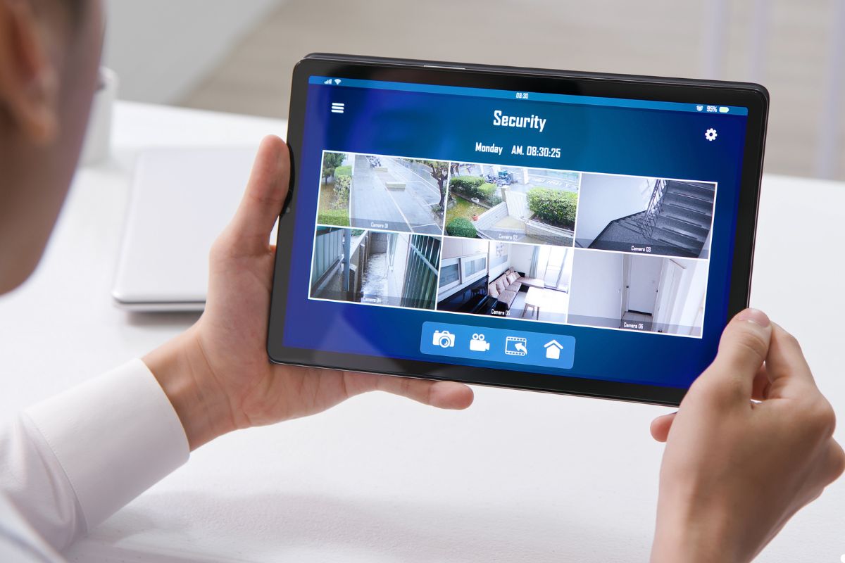 A man holding a tablet displaying a security camera feed, focused on monitoring the area.